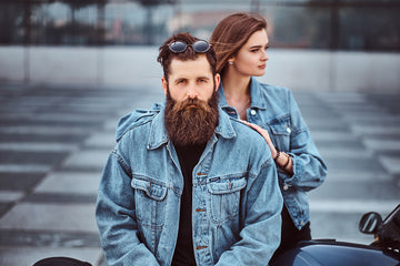 Close-up portrait of a hipster couple of a brutal bearded male and his girlfriend dressed in jeans jackets against skyscraper. - Wicked Beard Company