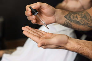 Hairdresser with beard oil near client in barbershop, closeup. Professional shaving service