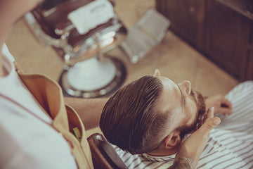 Man in a chair having wicked beard company beard oil applied to beard by barber
